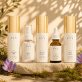The Complete Ritual: all five Hello Evy formulas, N° 01 to N° 05, on a stone plinth with moss, saffron crocus and wildflowers