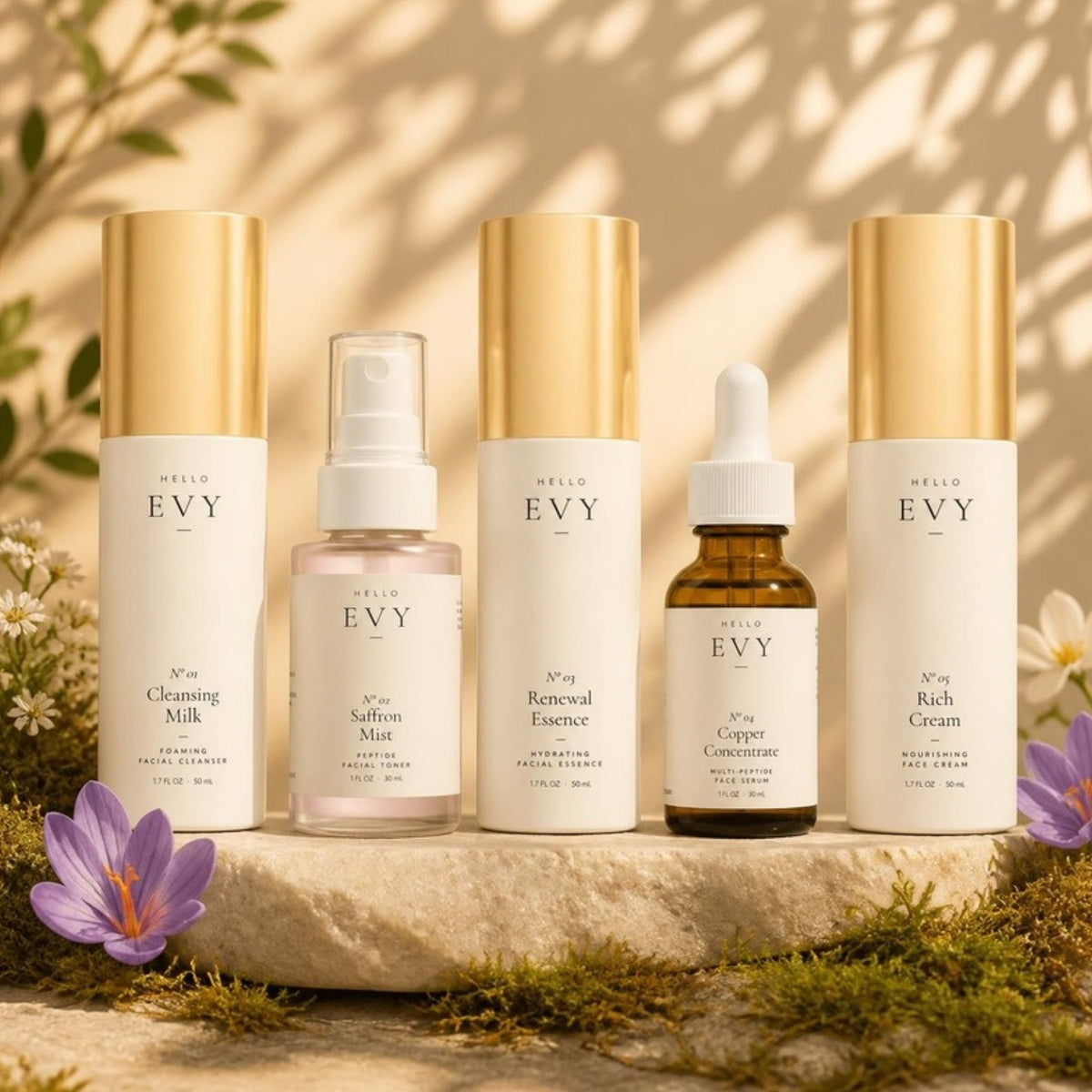 The Complete Ritual: all five Hello Evy formulas, N° 01 to N° 05, on a stone plinth with moss, saffron crocus and wildflowers